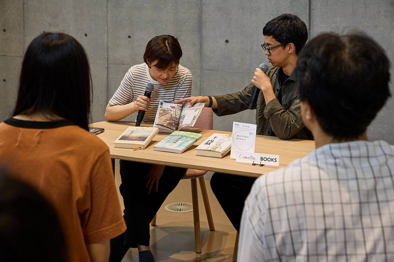 Scene from the ‘Hito to Nari Books’ event. Two speakers holding microphones introduce books while the audience watches.