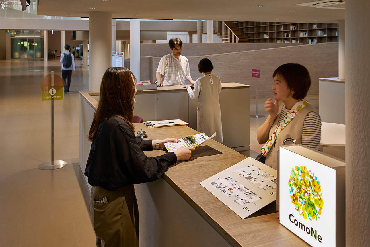 At the information counter, crew members greet visitors with smiles while providing guidance and handing out materials.