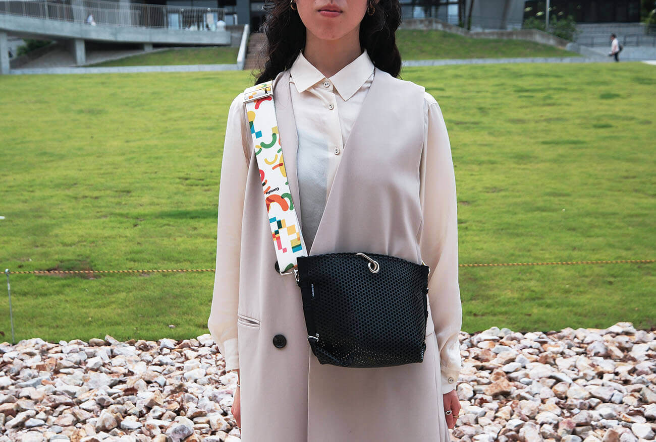 Front view of a uniform featuring a shoulder strap adorned with ComoNe's symbol pattern. Worn outdoors with a black bag slung over the shoulder.