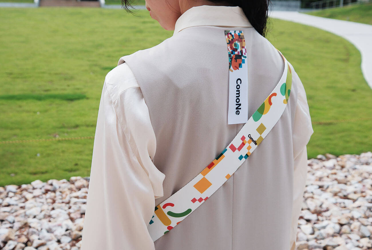 Back view of a uniform featuring a shoulder strap adorned with ComoNe's symbol pattern. Worn outdoors with a black bag slung over the shoulder.