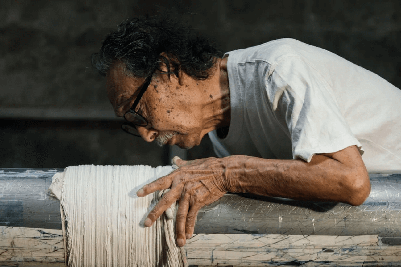 嵐絞りの工程。早川嘉英さんが白い布を棒にらせん状に巻き付け、指先で強く絞り込んで模様を仕込んでいる瞬間。