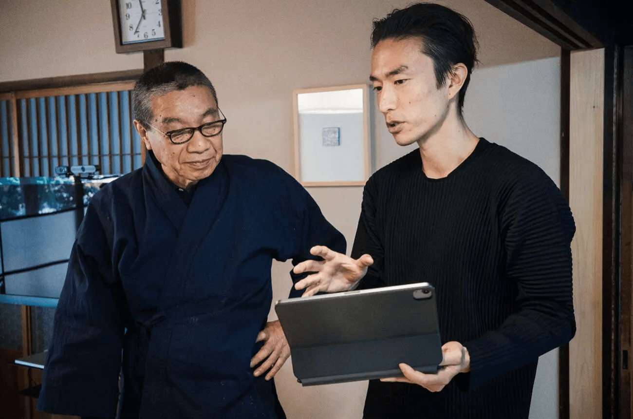 有松鳴海絞りの4代目職人・村瀬裕さん（左）が、デンソーのプロジェクト担当者吉岡裕記さん（右）のタブレット画面を覗き込みながら、アーカイブ手法について意見交換している。