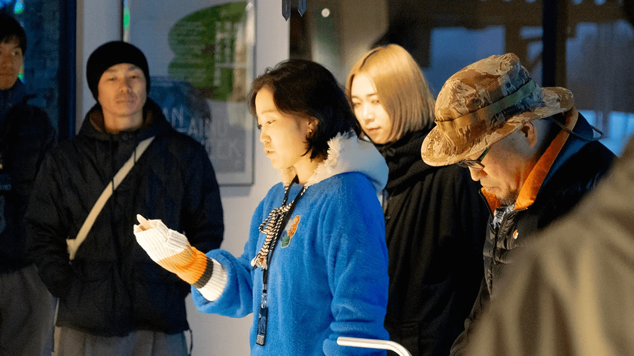 人々がアートを鑑賞している様子。青い服の若い女性が作品らしきものに手を翳している。