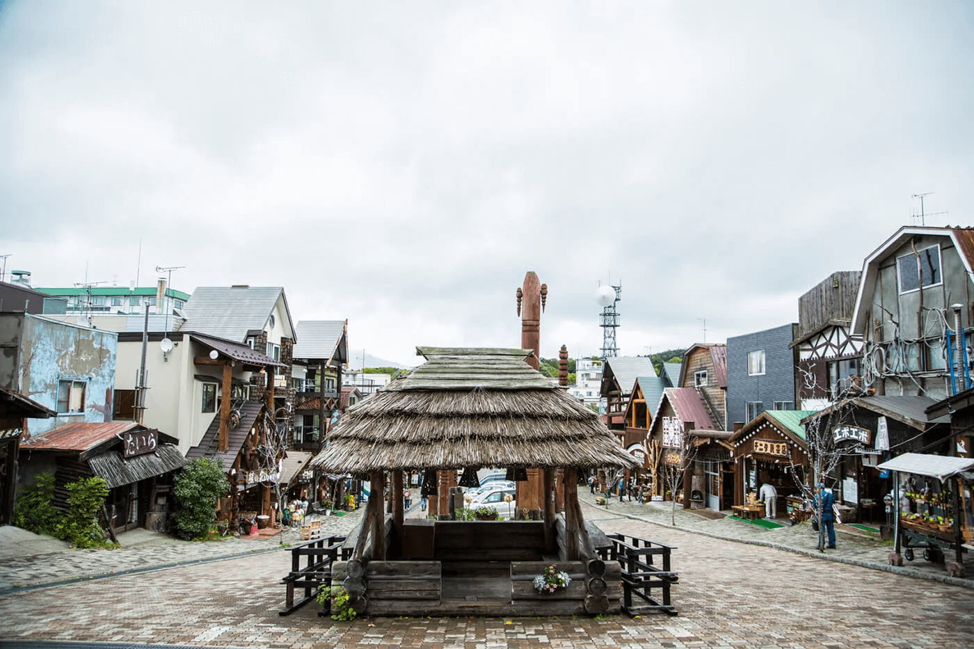 阿寒湖アイヌコタンの象徴的な風景写真。道の真ん中に東屋があり、両脇にアイヌ料理を出す飲食店や土産物屋などが並んでいる。