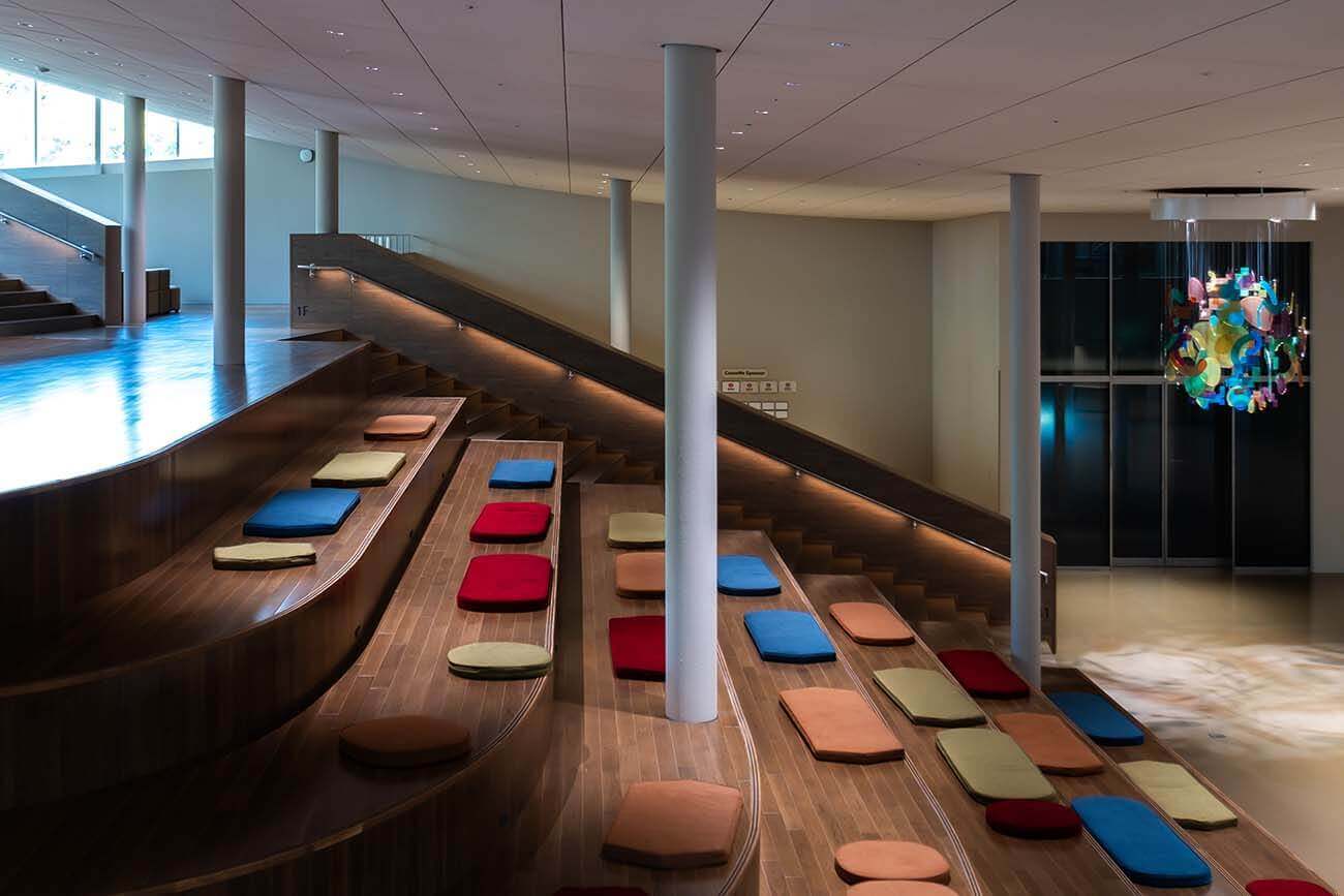 大階段の座面にカラフルなクッションが並べられ、利用者が快適に座れるように整えられている。奥には吊り下げオブジェが見える。