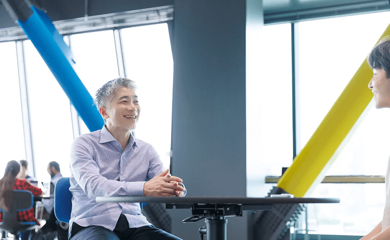 大きな窓から光が差し込む共創施設で、諏訪光洋が聞き手に向かって笑顔を見せている