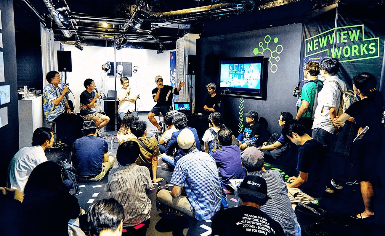 NEWVIEWプロジェクトのイベントで、登壇者がマイクを手に語り、観客がスクリーンを見ながら耳を傾けている様子