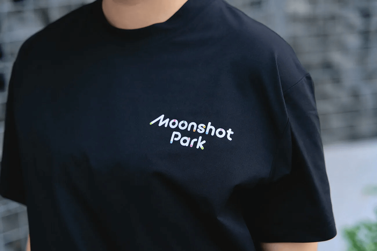 胸元に「Moonshot Park」のロゴが入った黒いTシャツを着るスタッフ。展示の統一的なビジュアルアイデンティティを示すユニフォームの一部。